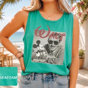 Peut inclure: Un d&eacute;bardeur sans manches vert mousse arborant une impression graphique de Walt Disney portant des lunettes de soleil &agrave; c&ocirc;t&eacute; de Mickey Mouse. Le mot Walt est imprim&eacute; dans une police rouge stylis&eacute;e au-dessus de l'image en noir et blanc.