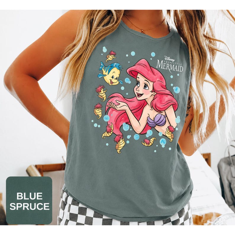 Peut inclure: Un d&eacute;bardeur sans manches bleu &eacute;pic&eacute;a avec une impression graphique d'Ariel de La Petite Sir&egrave;ne aux longs cheveux rouges, un haut coquillage violet et Polochon le poisson, entour&eacute;s de petits hippocampes et de bulles bleues avec le logo du film.