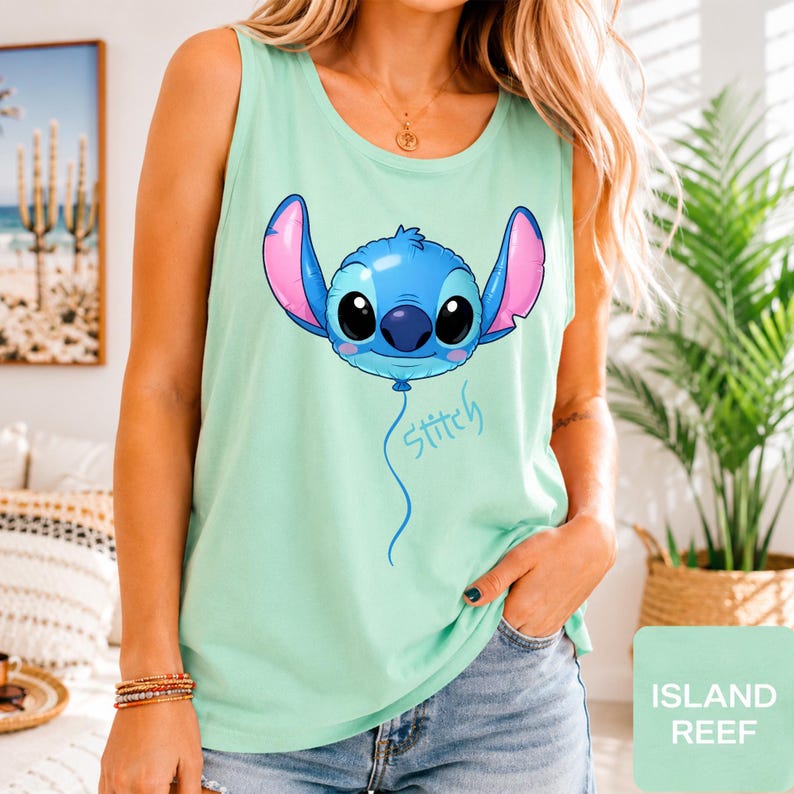 May include: A light mint green sleeveless tank top featuring a graphic of a blue character head shaped like a balloon with large black eyes and pink inner ears, with the word Stitch written in a cursive blue font below the balloon graphic.