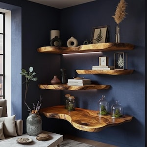 May include: Wooden floating shelves with a live edge design are mounted on a dark blue wall. The shelves display decorative vases, books, framed art, and glass cloches with plants. A modern interior design concept.