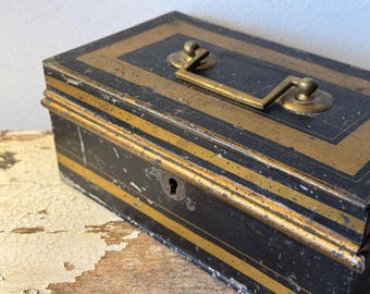 May include: A vintage black metal cash box with gold stripes and a brass handle. The box has a keyhole and is slightly worn.