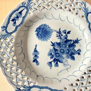 May include: A white ceramic plate with a blue and white floral design. The plate has a decorative openwork border.