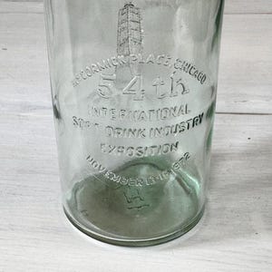 May include: Clear glass bottle with embossed text: "McCormick Place, Chicago 54th International Soft Drink Industry Exposition November 13-16 1972". The bottle has a cylindrical shape and a slightly green tint.