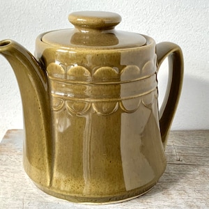 May include: A green ceramic teapot with a lid and a decorative scalloped design around the body.