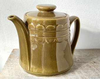 May include: A green ceramic teapot with a lid and a decorative scalloped design around the body.