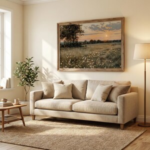 K&ouml;nnte beinhalten: Ein Wohnzimmer mit beigem Sofa, passenden Kissen, einem gerahmten Landschaftsbild, einem Jute-Teppich und einer Stehlampe. Ein kleiner Beistelltisch mit B&uuml;chern und Tassen steht neben einer Topfpflanze. Der Raum hat eine warme, einladende Atmosph&auml;re.