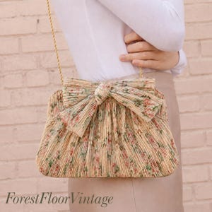 Lifestyle image of Loeffler Randall Tan Vine Floral pleated bow clutch worn as a wedding guest bag with gold chain strap.
