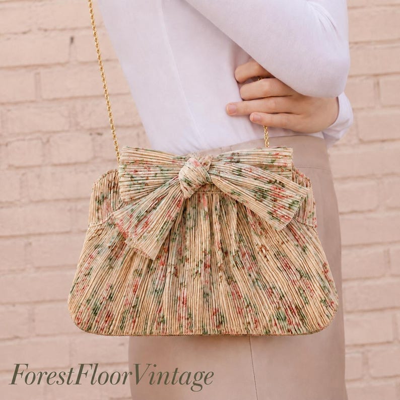 Lifestyle image of Loeffler Randall Tan Vine Floral pleated bow clutch worn as a wedding guest bag with gold chain strap.