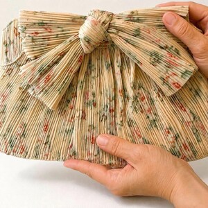 Close-up of Loeffler Randall Rayne Tan Vine Floral clutch held by hand showing full-size scale and pleated bow detail.
