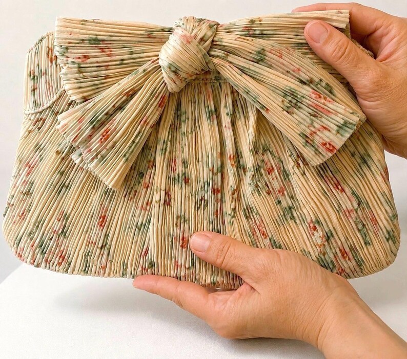 Close-up of Loeffler Randall Rayne Tan Vine Floral clutch held by hand showing full-size scale and pleated bow detail.