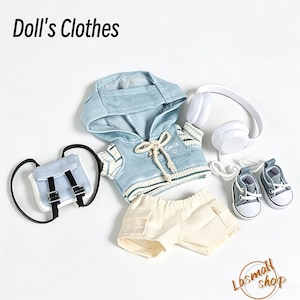 May include: A set of doll's clothing, featuring a light blue hoodie, cream shorts, a small backpack, white headphones, and grey and white trainers. The image includes the text "Doll's Clothes" at the top.