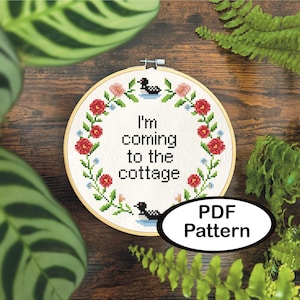 May include: A cross-stitch embroidery hoop with the text "I'm coming to the cottage." The design includes red and pink flowers, green leaves, and two black and white loon figures. A white oval with "PDF Pattern" is in the lower right.