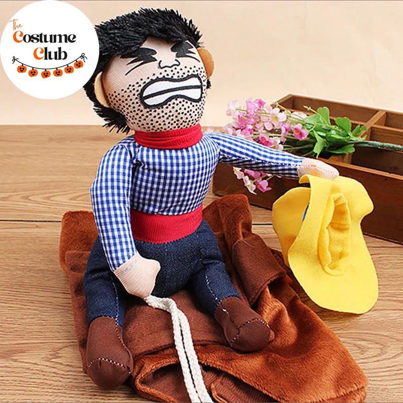 May include: A plush costume depicting a person riding a bucking bronco. The costume features a blue and white checkered shirt, denim pants, and brown boots. A yellow hat sits nearby. The Costume Club logo is in the upper left corner.