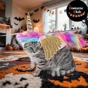 May include: A gray tabby cat wearing a unicorn costume with a gold horn, rainbow mane, and gold wings. The cat is sitting on a Halloween-themed rug with jack-o'-lanterns and other decorations. The Costume Club logo is in the background.