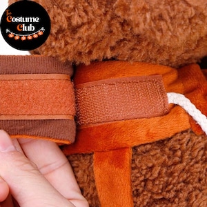 May include: Close-up of a brown and orange costume with a hook and loop fastener. The Costume Club logo is in the upper left corner. The costume appears to be made of a soft, plush material.