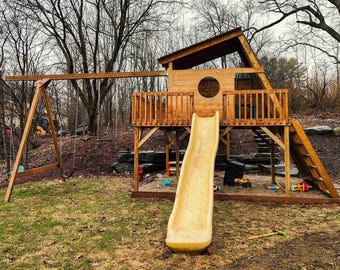 May include: A wooden playset featuring a swing set and a playhouse with a slide. The playhouse has a circular window and a ladder. The slide is yellow. The playset is on grass.