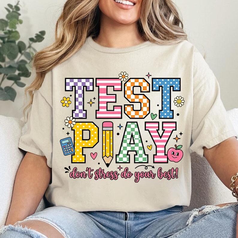 Puede incluir: Camiseta beige con las palabras "TEST PLAY" en letras coloridas y estampadas. El dise&ntilde;o incluye un l&aacute;piz, una calculadora, una manzana y la frase "don't stress do your best!" en una fuente divertida.