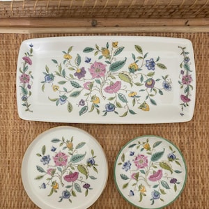 May include: A set of three floral patterned serving dishes. The set includes a rectangular platter and two round plates. The dishes feature a white background with pink, blue, yellow, and green floral designs. The round plates have gold and green rims.