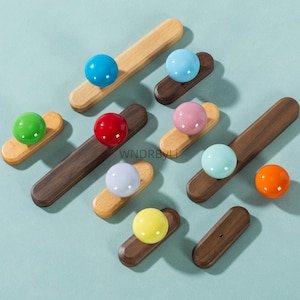 May include: A collection of wooden cabinet knobs with colorful spherical handles. The knobs are in various colors, including blue, green, red, pink, and yellow. The wooden bases are either light or dark brown.