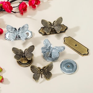 May include: A collection of decorative butterfly-shaped cabinet knobs and pulls in various metallic finishes, including silver and antique brass. The butterfly designs are detailed and three-dimensional, with a variety of base shapes and sizes.