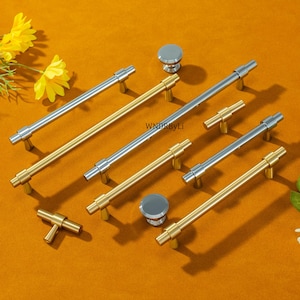 Könnte beinhalten: Eine Auswahl an Schrankbeschlägen, darunter silber- und goldfarbene Stangengriffe und runde Knöpfe. Die Hardware ist auf einer orangefarbenen Oberfläche angeordnet, mit einigen Teilen in gebürsteter Goldausführung und anderen in poliertem Silber. Der Text "WNDRByLi" ist sichtbar.