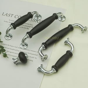 May include: A collection of black and silver cabinet hardware. The handles have a matte black center and curved silver accents. A matching knob is also included. The hardware is displayed on a white surface with text.