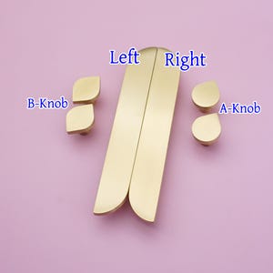 May include: Brass-coloured cabinet hardware set, including two long, curved handles labelled "Left" and "Right", and two sets of knobs labelled "B-Knob" and "A-Knob". The hardware is displayed on a light purple background.
