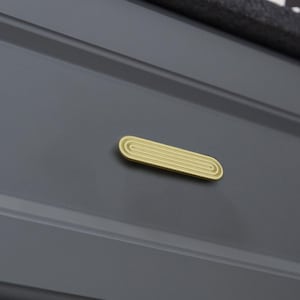Op de afbeelding: Een goudkleurige, ovaalvormige kastgreep met een groefontwerp. De greep is gemonteerd op een donkergrijze kastdeur. De hardware heeft een strakke, moderne esthetiek, geschikt voor diverse meubelstijlen.