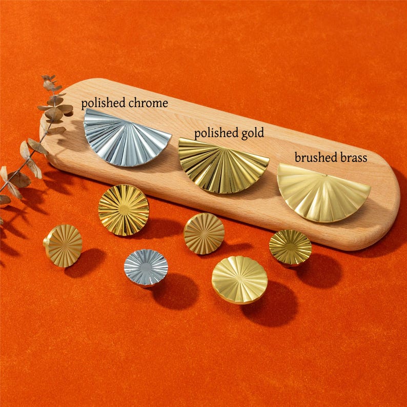 May include: A collection of decorative cabinet hardware in polished chrome, polished gold, and brushed brass finishes. The hardware includes half-circle and round designs. The text on the wooden board reads "polished chrome", "polished gold", and "brushed brass".