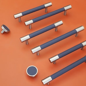 May include: A collection of cabinet hardware, including several long, navy blue and silver bar pulls and two matching round knobs. The hardware is arranged on an orange surface.