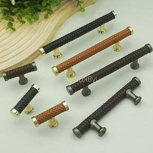 May include: A collection of decorative cabinet pulls and handles. The pulls feature a braided leather design in various colors, including black, brown, and tan. The hardware has gold and silver accents.