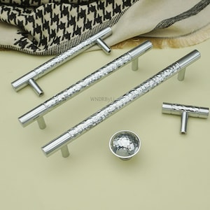 May include: A collection of silver cabinet hardware, including T-bar handles, long bar pulls, and a round knob. The hardware has a hammered texture and a polished finish, suitable for kitchen or bathroom cabinets.