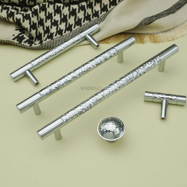 May include: A collection of silver cabinet hardware, including T-bar handles, long bar pulls, and a round knob. The hardware has a hammered texture and a polished finish, suitable for kitchen or bathroom cabinets.