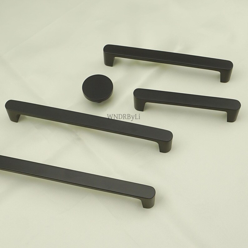 May include: A collection of matte black cabinet hardware, including several bar pulls and a round knob. The pulls vary in length, offering options for different cabinet sizes. The hardware is designed with a modern, minimalist aesthetic.