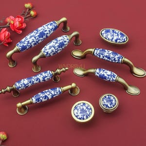 May include: A collection of cabinet hardware with a blue and white floral design on a white background. The hardware includes various sizes of handles and knobs with a brass finish. The items are arranged on a red surface.