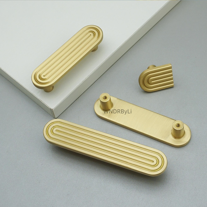 Op de afbeelding: Goudkleurige kastbeslagset. De set bevat verschillende rechthoekige handgrepen met een groefontwerp, een kleine knop en een rechthoekig stuk met twee schroefgaten. De hardware is gemaakt van metaal en heeft een matte afwerking.