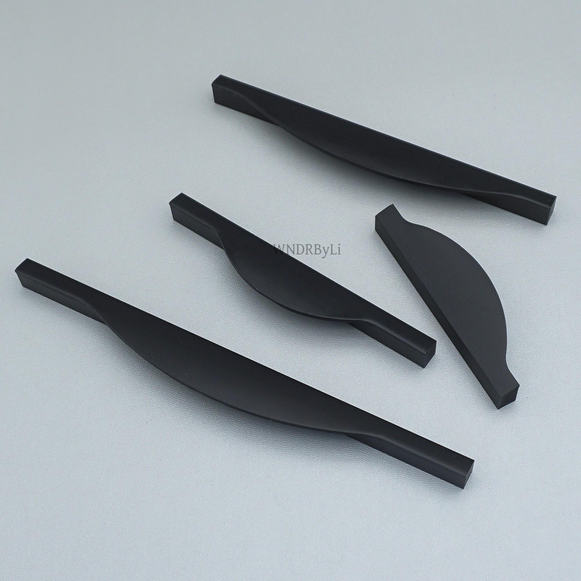 May include: Four matte black cabinet pulls with a twisted, curved design. The pulls have a rectangular shape at each end and a smooth, ergonomic curve in the center. The hardware is designed for easy installation and a modern aesthetic.