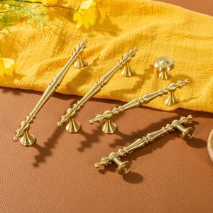 Peut inclure: Ensemble de quincaillerie de meubles en laiton de style antique, comprenant des poign&eacute;es et un bouton. Les poign&eacute;es pr&eacute;sentent des d&eacute;tails orn&eacute;s et sont pr&eacute;sent&eacute;es sur un tissu jaune. Id&eacute;al pour la d&eacute;coration int&eacute;rieure.