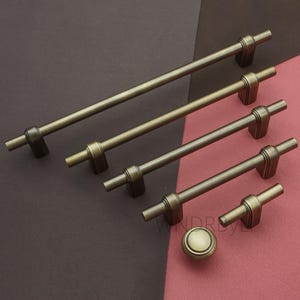 May include: A collection of antique brass cabinet hardware, including several bar pulls and a round knob. The hardware has a vintage aesthetic, with a warm, aged finish. The pulls vary in length, offering options for different cabinet sizes.