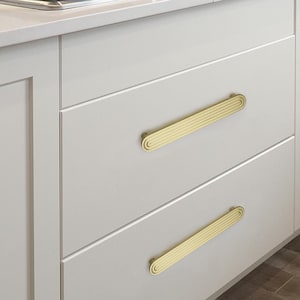 Op de afbeelding: Close-up van een keukenkast met twee lades. Elke lade heeft een goudkleurige, gegroefde handgreep. De kastdeuren zijn lichtgrijs en de handgrepen zijn horizontaal uitgelijnd.