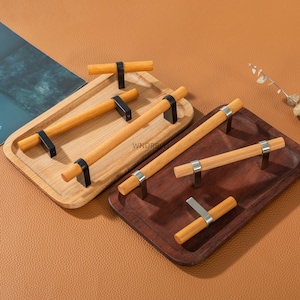 May include: A collection of wooden cabinet handles with metal accents. The handles are displayed on two wooden trays, one light-colored and one dark. The handles have a cylindrical design with black or silver metal hardware.