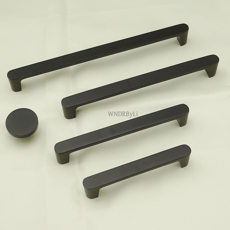 May include: A set of matte black cabinet hardware, including four rectangular handles of varying lengths and a round knob. The hardware is made of metal and has a modern, minimalist design. The text "WNDRByLi" is visible on the image.