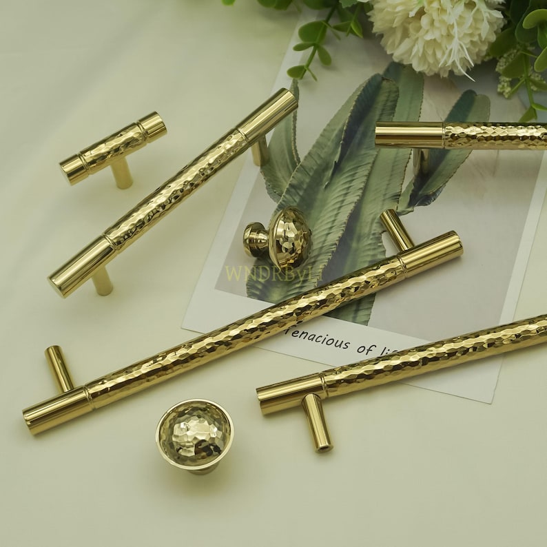May include: A collection of gold-colored cabinet hardware, including bar pulls and knobs. The hardware has a hammered texture and a bright, reflective finish. The set includes various sizes and styles for different cabinet configurations.