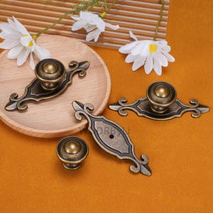 May include: Antique bronze cabinet hardware set. Includes two ornate pulls with round knobs and two matching knobs. The hardware features a dark bronze finish with decorative scrollwork. Perfect for adding a vintage touch to furniture.