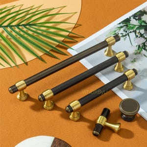 May include: A collection of cabinet hardware featuring dark brown and gold finishes. The set includes several bar pulls, a knob, and a smaller pull. The hardware has a cylindrical design with gold accents and a dark brown center.