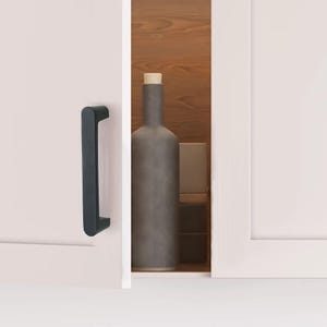 May include: A black cabinet pull handle is mounted on a white cabinet door. The handle is a simple, modern design. Inside the cabinet, a gray bottle with a cork top and a small, square container are visible.