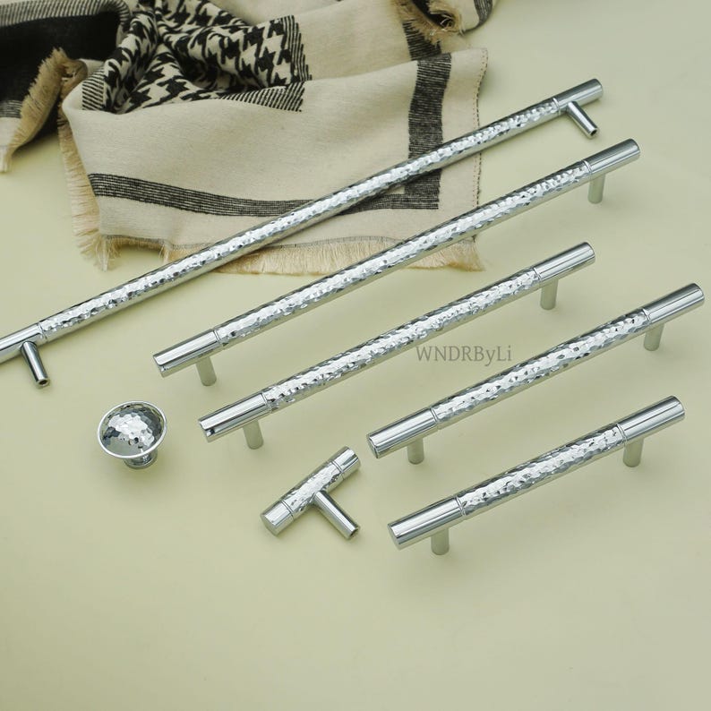 May include: A collection of silver cabinet hardware, including several bar pulls, a knob, and a T-shaped pull. The hardware has a hammered texture and a polished finish. The pulls vary in length.