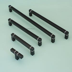 May include: A set of black cabinet handles in different lengths. Each handle has a rectangular shape with a matte finish and is decorated with small, sparkling details at the ends. The handles are displayed on a light green background.