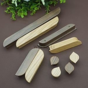 May include: A collection of wooden cabinet hardware, including handles and knobs. The handles are in various shapes and sizes, with a mix of light and dark wood tones. The knobs have a teardrop and diamond shape. The text "WNDRBYLi" is visible.