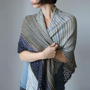 May include: A knitted shawl in shades of blue, grey, and yellow. The shawl has a striped pattern with a dark blue border and a delicate lace edge. The garment is draped over the shoulders.